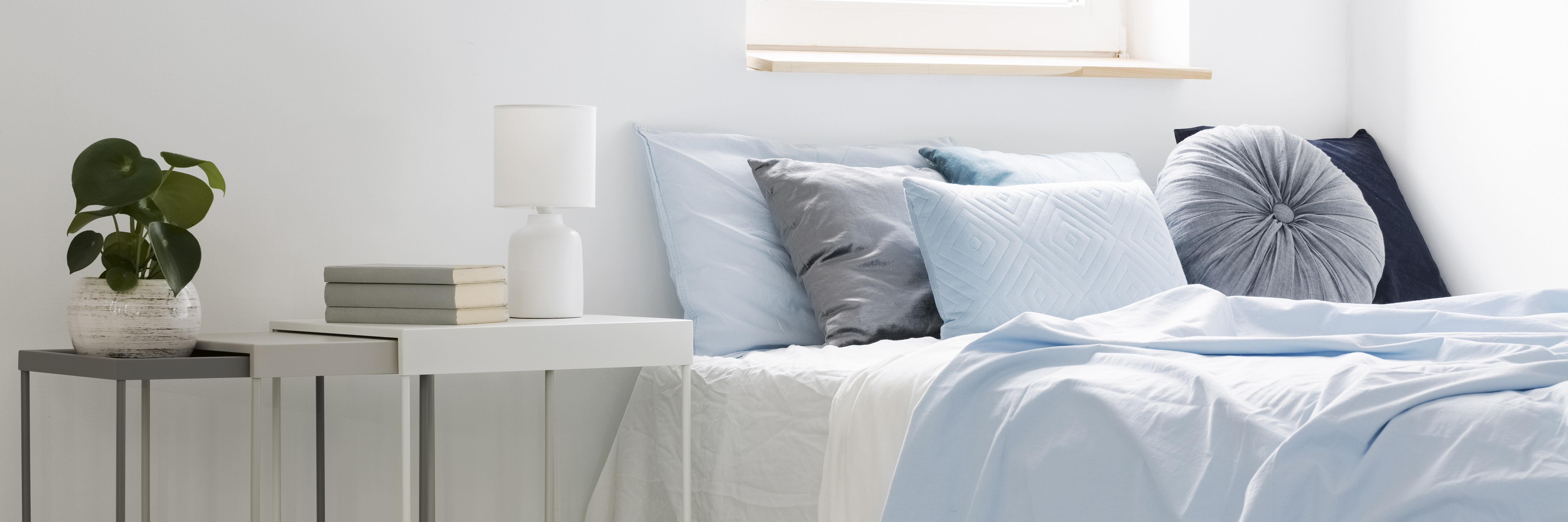 bed with blue bedding and cushions standing next to white tables with books