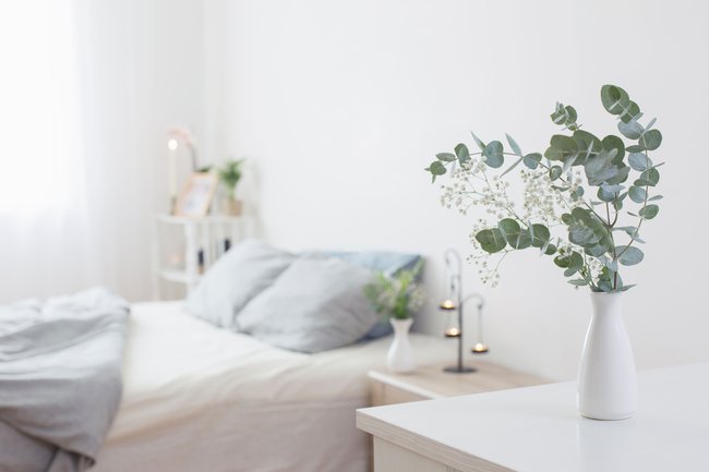 eucalyptus and gypsophila in vase in white bedroom with gold accents in background